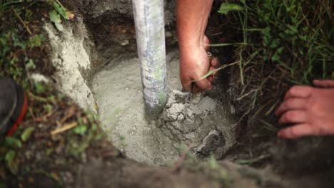Worker-uses-concrete-trowel-to-spread-mixture-around-steel-pipe-dug-into-ground
