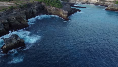 Nusa-Ceningan's-Blue-Lagoon-and-Coastal-Cliffs-with-Ocean-Waves-in-Indonesia-from-an-Aerial-Drone-Tilt-Down