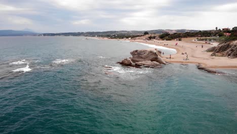 Drone-video-passing-over-rock-formation-sea-waves-crashing-people-swimming-summer