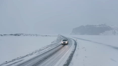 Vista-Aérea-Hacia-Atrás-Frente-A-Un-Todoterreno-Conduciendo-Por-Una-Carretera-Nevada,-Tormenta-De-Nieve-En-Islandia