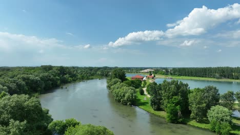 Aerial-drone-footage-ascends-above-the-Small-Danube-river,-unveiling-gravel-pits,-pristine-emerald-lakes,-and-picturesque-fields-below