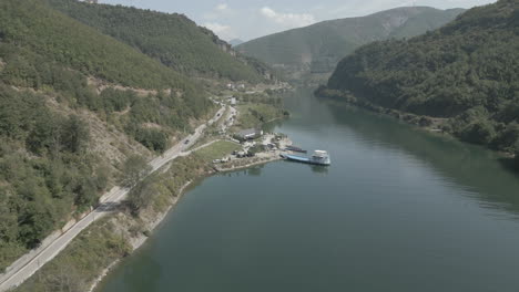 Drone-shot-flying-over-the-ferry-stop-in-Fierze-Albania-with-a-boat-and-ferry-in-the-water-loading-passengers-on-a-sunny-day-LOG