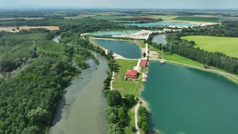 Aerial-ascending-drone-footage-of-the-Small-Danube-river-revealing-gravel-pits,-emerald-lakes-and-fields-below