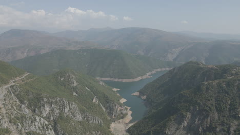 Drohnenschuss,-Der-An-Einem-Sonnigen-Tag-Mit-Wolken-Mit-Blauem-Wasser-Und-Einem-Grünen-Talstamm-über-Die-Berge-In-Der-Nähe-Des-Koman-Sees-In-Albanien-Fliegt