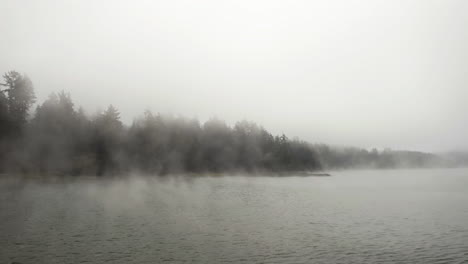 Aerial-tracking-shot-low-over-water-surface-on-a-misty-lake,-cloudy-day-in-USA