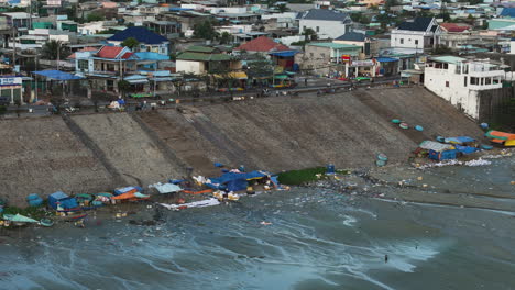 Mui-ne-fisherman-village-lined-with-plastic-marine-debris-on-shore-at-low-tide,-aerial-telephoto-pan