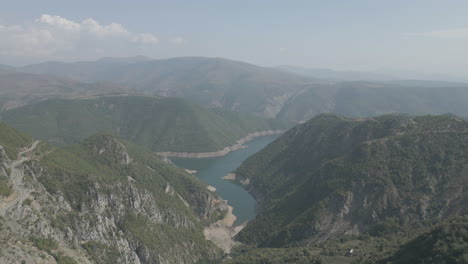Drohnenschuss,-Der-An-Einem-Sonnigen-Tag-Mit-Wolken-Mit-Blauem-Wasser-Und-Einem-Grünen-Talstamm-über-Die-Berge-In-Der-Nähe-Des-Koman-Sees-In-Albanien-Fliegt
