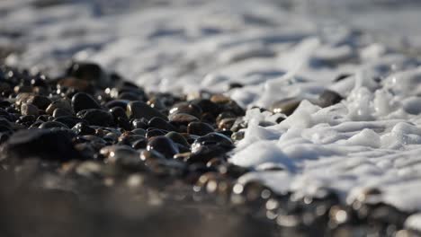 Ocean-waves-on-pebbles-beach,-Foamy-ocean-water,-Closeup