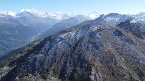 a-big-rock-in-front-of-snowy-mountains-ins-the-swiss-alps,-aerial-drone