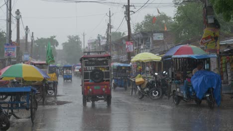 Heavy-rainfall-after-intense-heat-wave-in-the-rural-Indian-town,-E-rickshaws-parked-roadside-in-rainfall