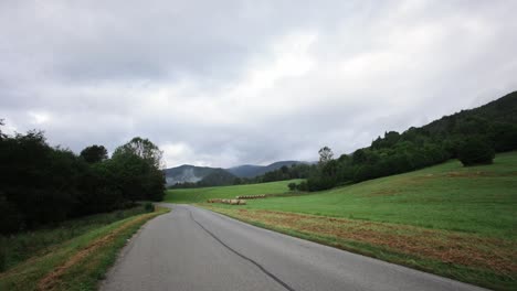 Empty-country-road-with-black-asphalt-line-with-grassy-hillside-and-foggy-mountains-in-distance