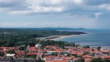 Telephoto-aerial-of-scenic-landscape-behind-rooftops-of-city-Simrishamn,-Sweden