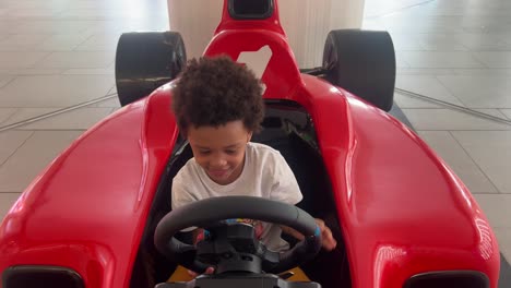 Niño-Negro-De-3-Años-Conduciendo-Un-Coche-De-Juguete-Rojo-F1-Dentro-De-Un-Centro-Comercial