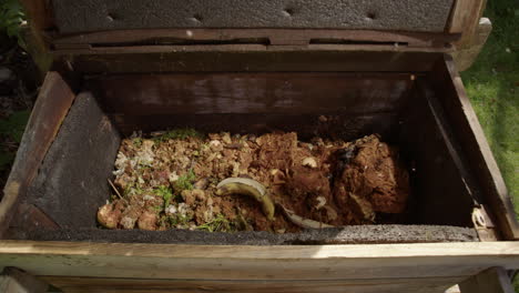 Wooden-composting-bin-opened-and-organic-food-waste-dumped-inside,-slow-motion