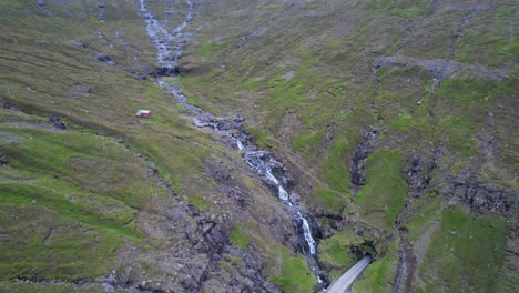 Cars-drive-into-tunnel-next-to-cascading-waterfalls-and-streams-near-Arnafjordur,-Faroe-Islands