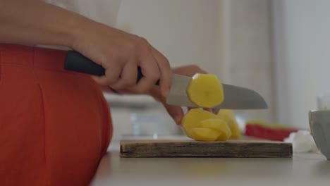 Static,-close-up-of-a-woman-cutting-potatoes-with-a-chef-knife-in-a-tiny-kitchen-during-midday