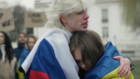 Young-caucasian-man-with-Russian-flag-hugging-young-caucasian-woman-with-Ukrainian-flag.