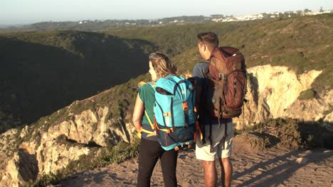 Couple-of-tourists-with-camping-backpacks-standing-at-cliff