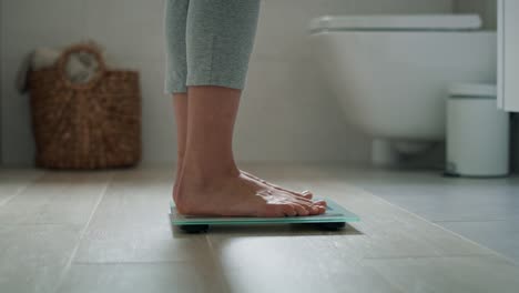 Legs-of-unrecognizable-woman-stepping-on-the-bathroom-scale.