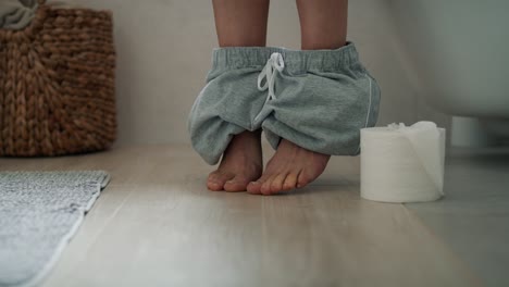 Detail-of-legs-of-woman-sitting-on-toilet-and-holding-a-toilet-paper-roll.
