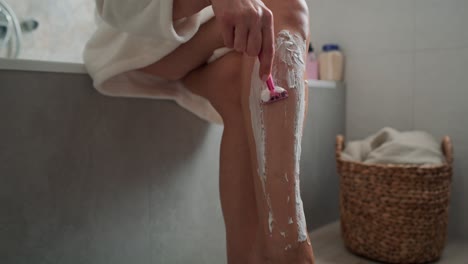 Caucasian-woman-in-bathrobe-shaving-her-legs.