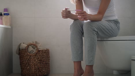 Stressed-unrecognizable-woman-sitting-on-toilet-and-waiting-for-pregnancy-test-results.