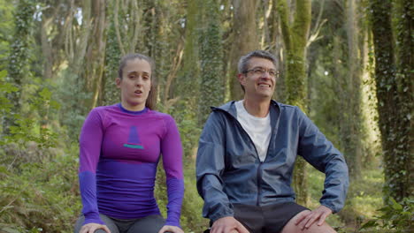 Man-and-woman-sitting-and-resting-after-trail-running-in-forest