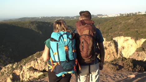 Couple-with-camping-backpacks-standing-at-cliff