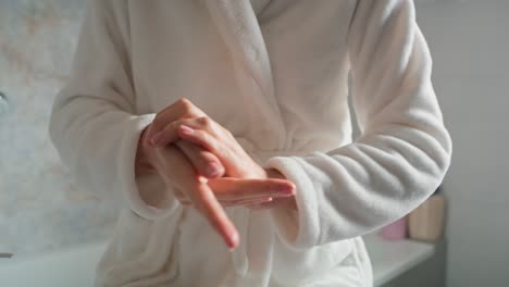 Unrecognizable-woman-in-bathrobe-applying-moisturizing-cream-on-hands.
