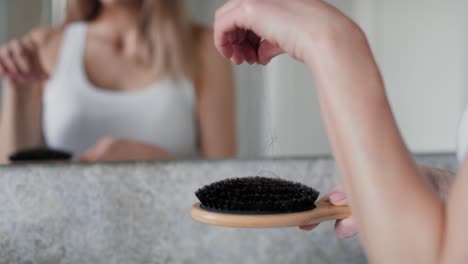 Caucasian-woman-brushing-hair-in-the-bathroom-and-looking-at-their-loss-on-the-brush.