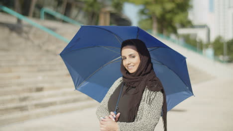 Young-muslim-woman-in-hijab-hiding-under-umbrella-on-sunny-day.