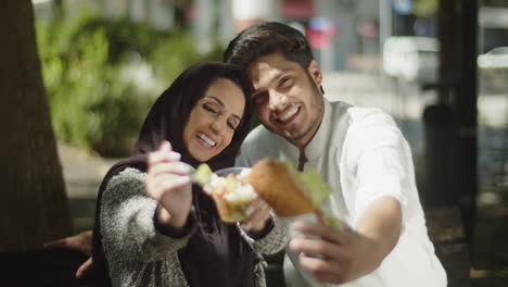 Young-muslim-couple-showing-their-lunch-to-camera-and-eating-it.