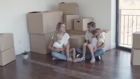 Eltern-Und-Zwei-Mädchen-Sitzen-Auf-Dem-Boden-Neben-Kisten