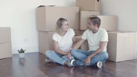 Cheerful-couple-sitting-on-floor-near-heap-of-boxes