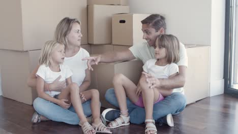 Family-couple-and-two-girls-sitting-on-floor-near-boxes
