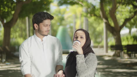 Lovely-muslim-couple-walking-in-park,-drinking-takeaway-coffee.