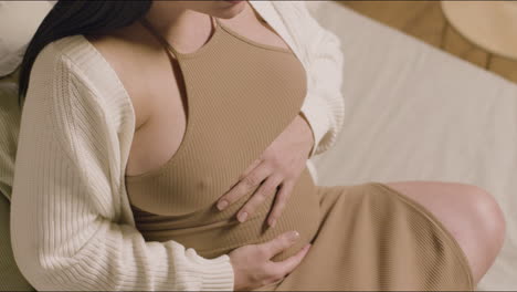 Pregnant-woman-sitting-on-bed-and-touching-tummy
