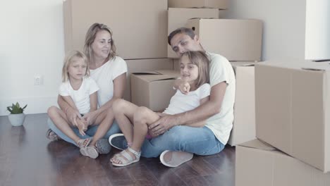 Parents-and-two-daughters-sitting-on-floor-near-boxes