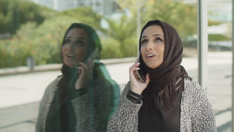 Junge-Muslimische-Frau-Lehnt-An-Einer-Reflektierenden-Wand-Und-Telefoniert.