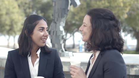 Brunette-businesswomen-drinking-coffee-outdoors-and-talking