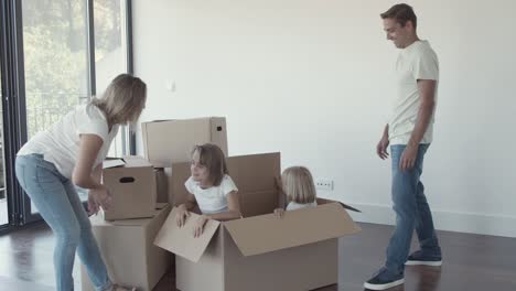 Parents-opening-big-cartoon-box-with-cheerful-daughters-inside