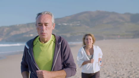 Focused-man-and-woman-running-along-ocean-coast-on-summer-day