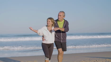 Cheerful-elderly-man-and-woman-hugging-and-walking-along-ocean