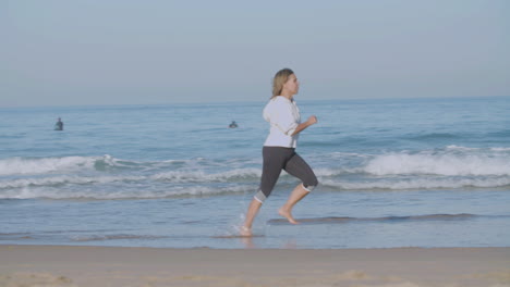 Concentrated-woman-running-barefoot-fast-along-ocean-coast