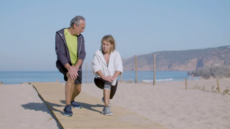Mature-couple-lunging-forward-on-wooden-path-on-sandy-seashore
