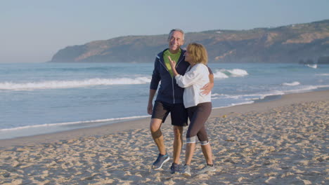 Happy-elderly-couple-hugging-and-walking-along-ocean-coast