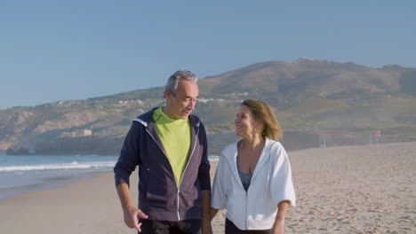 Mature-couple-holding-hands-and-walking-along-ocean-coast