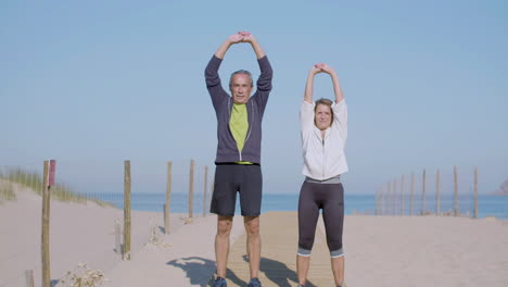 Focused-elderly-couple-exercising-on-sandy-beach-on-summer-day