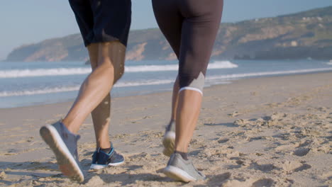 Man-and-woman-in-sportswear-and-sneakers-running-on-sandy-beach