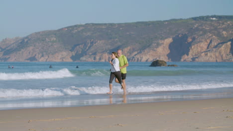 Happy-mature-couple-running-barefoot-on-sandy-beach